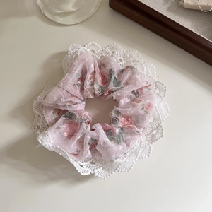 Détail d'un chouchou en mousseline florale avec dentelle blanche et motifs roses