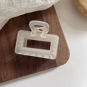 Détail d'une pince à cheveux rectangulaire blanc mat avec ressort en métal doré