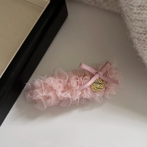 Dettaglio del fermaglio in pizzo rosa con fiocco dorato e targhetta in metallo lucido