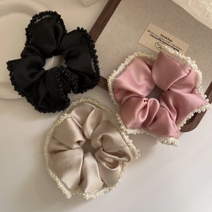 Detailed view of three satin scrunchies with bead edges in black, pink, and champagne gold