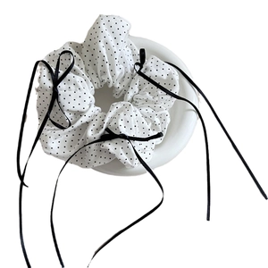 Elegant white polka dot scrunchie with long black ribbons on a minimalist white tray