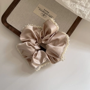 Detail of champagne satin scrunchie with white pearl trim for elegant hair styling