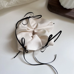 Nahaufnahme von cremefarbenem Satin-Scrunchie mit schwarzen Schleifen und weicher Textur