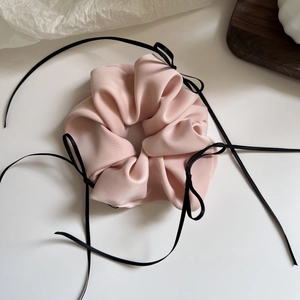 Detail eines rosa Satin-Haargummis mit schwarzen Bandschleifen auf weißem Grund