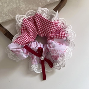 Close-up of a plaid floral scrunchie with lace trim, ribbon bow, and white faux pearl detail