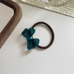 Détail du chouchou en acétate vert foncé avec lettrage doré sur fond blanc impeccable