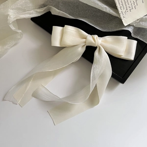 Detail of elegant cream satin bow hair clip with textured ribbon and long streamers