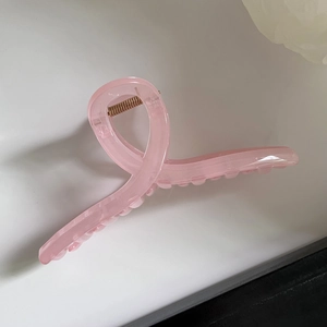 Detail of large pink jelly hair claw clip with glossy ribbon-like twist and metal spring