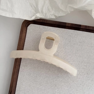 Détail d'une grande pince à cheveux crème mate avec ressort doré sur plateau en bois