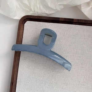Détail d'une pince à cheveux de 13 cm en acrylique bleu brillant sur un support en toile