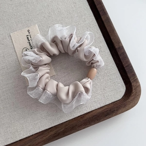 Detail of beige satin hair tie with white lace edges and wooden bead on a tray
