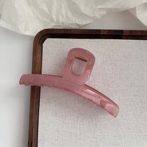 Détail d'une grande pince à cheveux rose translucide de 13 cm sur un plateau chic
