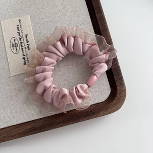 Detail of pink satin hair tie with delicate mesh lace edges on a wooden tray