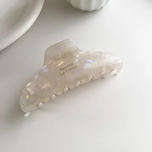 Vue macro d'une pince à cheveux en acétate blanc perle avec texte Barrette La France doré