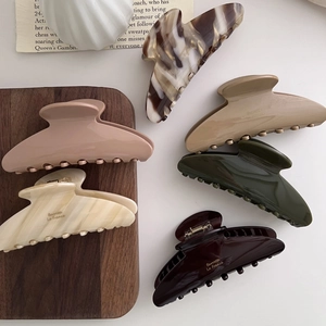 Close-up of large acetate hair claws in various elegant colors on a stylish wooden tray