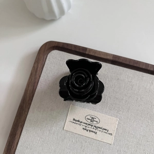 Détail d'une pince à cheveux rose noire en acétate posée sur un plateau en bois minimaliste