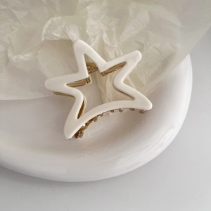 Macro shot of white matte star hair claw clip with golden metal spring on white plate