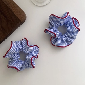 Close-up of two blue striped scrunchies with red stitched edges and soft cotton texture