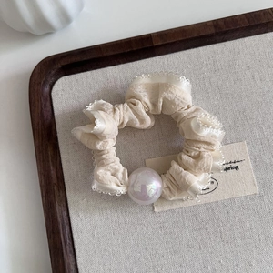 Detail of a beige lace scrunchie with iridescent pearl on a rustic wooden tray