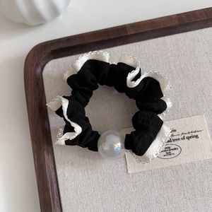 Detail of black scrunchie with white lace trim and iridescent pearl bead on wood tray