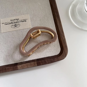 Detail of a brown acetate shark hair claw clip with golden metal frame on a wooden tray