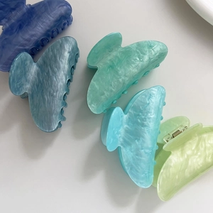 Dettaglio di varie pinze per capelli in acetato lucido verde e blu con trama marmorea