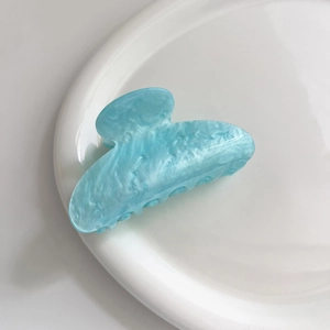 Dettaglio della molletta per capelli azzurra marmorizzata su un piatto di ceramica bianca
