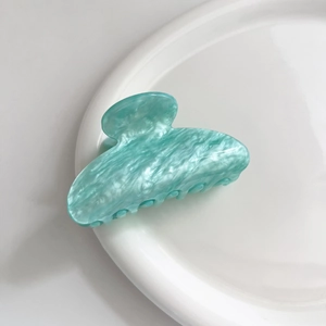 Dettaglio della molletta per capelli in acetato verde menta su un piatto bianco