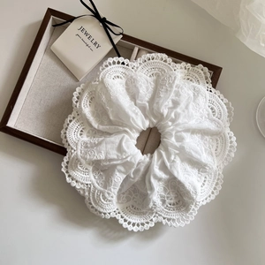 Close-up of white lace scrunchie with intricate embroidery texture and wavy edges