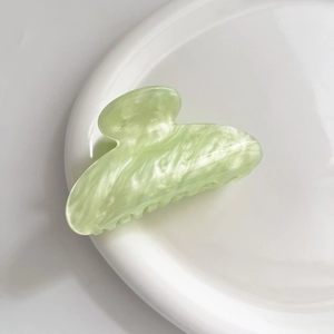 Dettaglio della pinza per capelli in acetato verde chiaro con trama marmorizzata lucida