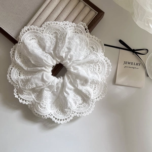 Elegant large white lace scrunchie with intricate floral hollow embroidery on a wooden stand