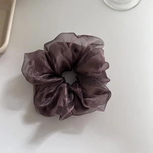 Macro detail of a dark purple double-layered sheer mesh scrunchie on a white tray