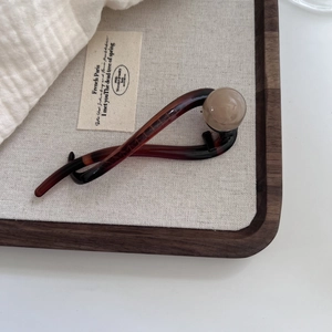 Elegant tortoiseshell brown hair clip with a pearl bead on a rustic wooden tray