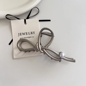 Detail shot of a matte silver metal hair claw featuring a pearl accent on white backdrop
