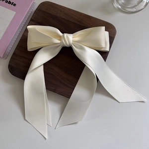 Elegant cream satin bow hair clip with long ribbons on a decorative wooden tray