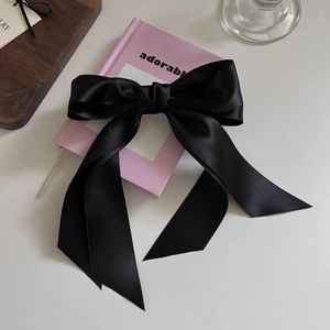 Elegant black satin bow hair clip with long ribbons on a pink decorative book