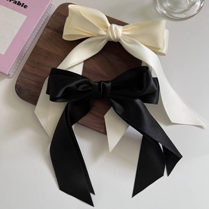 Detailed close-up of premium satin bow hair clips in cream white and classic black colors