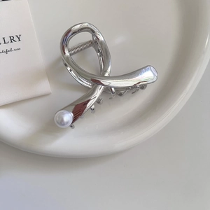 Silver metal cross hair claw clip with pearl on white ceramic tray in minimalist style