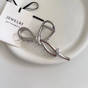 Elegant silver metallic bow hair claw clip with pearl accent on a ceramic dish