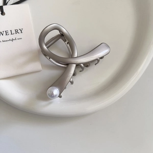 Minimalist matte silver cross hair claw clip with white pearl detail on ceramic plate