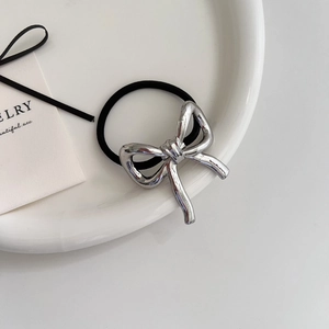 Minimalist silver metal bow hair tie with elastic rope on white ceramic tray