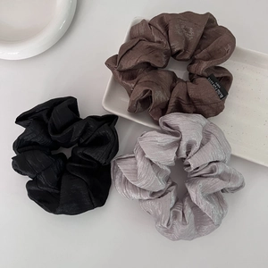 Close-up of pleated satin scrunchies in coffee, black, and lavender on a ceramic plate