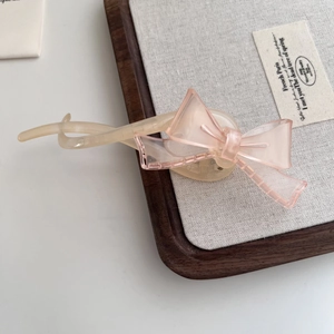 Détail d'une pince à cheveux beige translucide ornée d'un élégant nœud rose