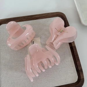 Detailed view of translucent pink resin hair claws in three shapes on a linen tray