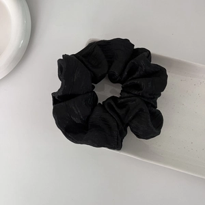Elegant black pleated scrunchie with a subtle silk sheen on a white ceramic tray