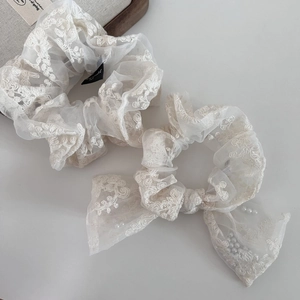 Detail of beige lace scrunchie and bow hair tie with floral embroidery and pearl accents