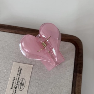 Glossy jelly pink heart hair claw clip with golden spring on a wooden stand