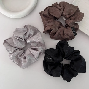 Close-up of pleated scrunchies set in brown, grey and black with shimmering fabric texture