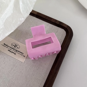 Pink square acetate hair claw clip with matte finish on a minimalist wooden tray