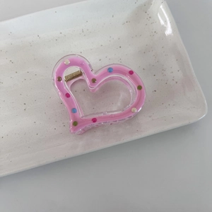 Gros plan d'une pince à cheveux coeur rose avec pois colorés sur un plateau en céramique